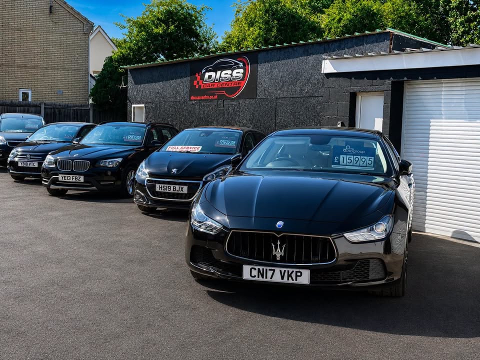 A row of cars on the sunny Diss Car Centre forecourt, a black Maserati at the front