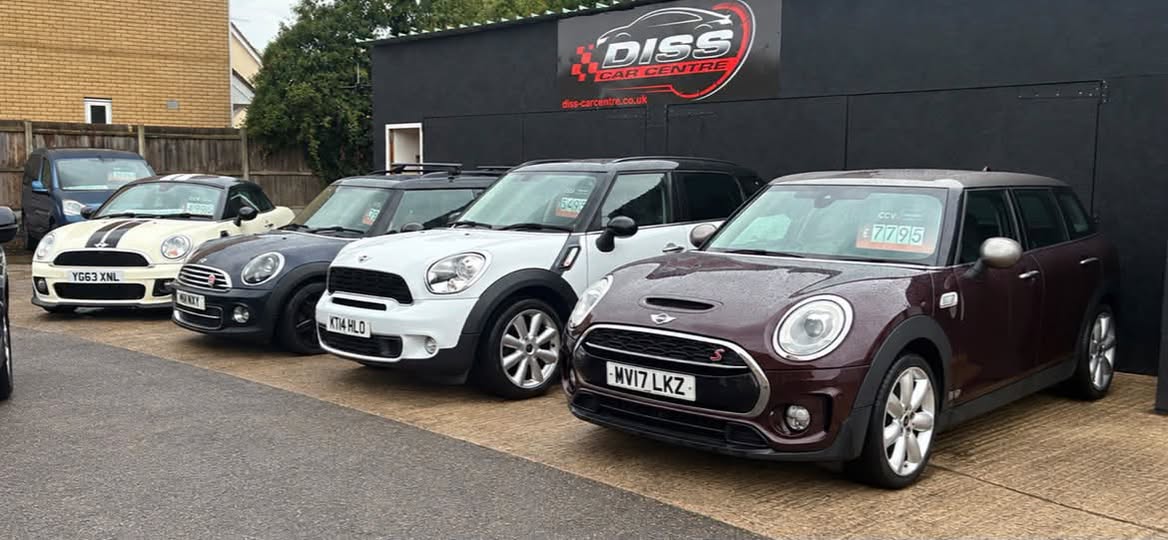 A row of MINIs, a Cooper, a Countryman and a Clubman, lined up in front of the Diss Car Centre sign