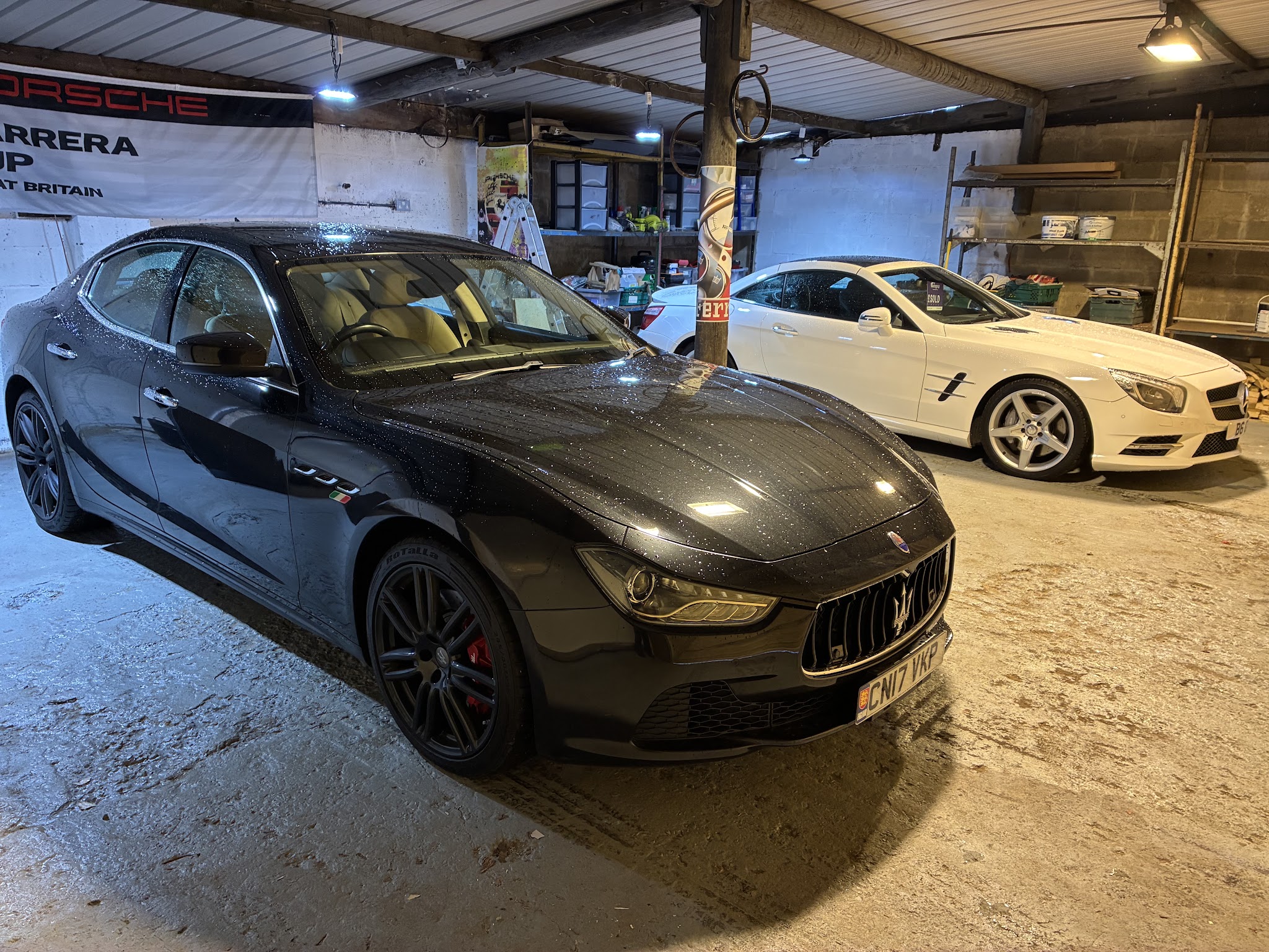 A freshly washed black Maserati Ghibli indoors at Diss Car Centre, a white Mercedes SL convertible behind